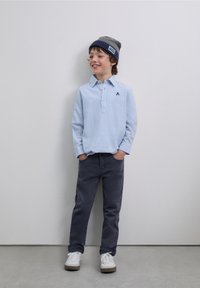 Ljusblå långärmad pikétröja med ränder och två knappar, mörkgrå byxor, grå och marinblå mössa och vita sneakers.