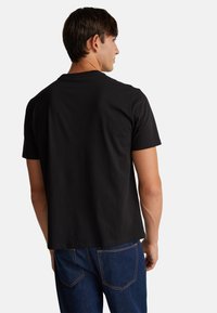 Černé tričko s krátkým rukávem z bavlny, které má pohodlný střih. Jednoduchý design s kulatým výstřihem, hladkou texturou a žádnými viditelnými logy nebo vzory.