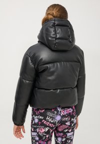 Giacca a vento nera con design imbottito e cappuccio, caratterizzata da una texture liscia e lucida. Abbinata a leggings colorati con motivo.