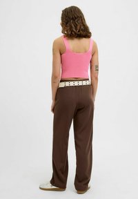 Ribotuotas rožinis be rankovių viršus derinamas su laisvomis rudos spalvos kelnėmis. Kelnės turi kreminės spalvos diržą su juodais taškais.