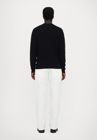 Pull en tricot noir avec un design texturé, associé à un pantalon large blanc. Le modèle est montré de dos.