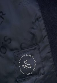 Der marinefarbene Stoff hat ein Pflegeetikett mit einem Herz- und Handgrafik, umgeben von Text auf einem kontrastierenden Hintergrund. Smooth Textur und modernes Design.