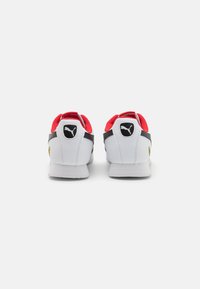 Sneaker bianche con accenti rossi, strisce nere e un logo sul tallone. Texture liscia e design arrotondato con una silhouette a profilo basso.