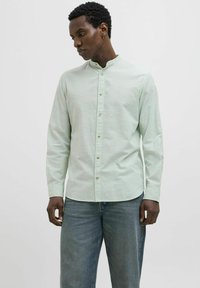 Cămașă butonată de culoare verde deschis, cu guler mandarin, mâneci lungi și țesătură texturată. Asortată cu blugi din denim albastru.