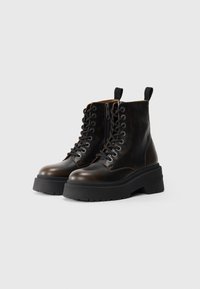 Bottines en cuir marron avec une semelle épaisse noire, à lacets, avec une fermeture éclair sur le côté et un tirette à l'arrière.