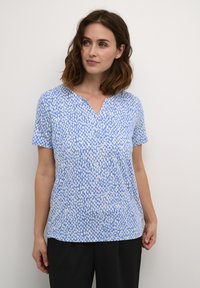 Blusa de manga corta en azul claro con un patrón abstracto en blanco, con un escote en V y un corte relajado. Tejido suave con una textura lisa.