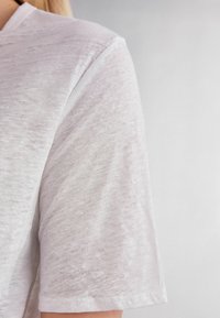 Hvid kortærmet t-shirt med et let, tekstureret stof og et subtilt heather-mønster, rund halsudskæring og løs pasform.