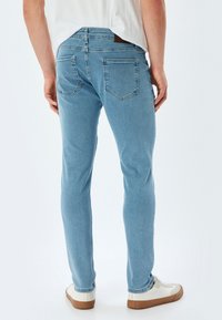 Jeans de denim de color azul claro con un ajuste slim, que cuentan con dos bolsillos traseros y una etiqueta de cuero en la cinturilla. Tejido texturizado y pierna entallada.