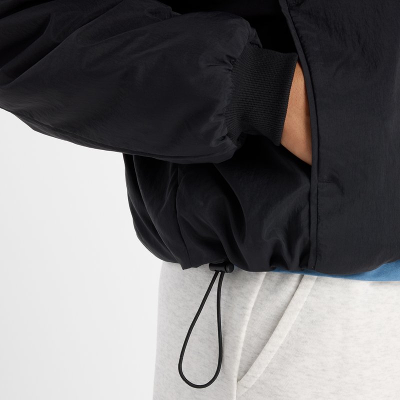 Black padded jacket with elastic cuffs and a drawstring hem, featuring a smooth texture and relaxed fit. Gray sweatpants visible underneath.