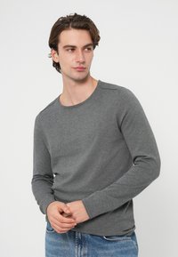 Siva majica z dolgimi rokavi iz mehke tkanine, z okroglim izrezom in oprijetimi manšetami. Izstopa po svoji preprosti, klasični zasnovi.