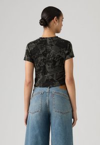 Μαύρο κοντομάνικο t-shirt με υφή γραφικού στη στάμπα, συνδυασμένο με ανοιχτό μπλε τζιν παντελόνι φαρδιάς γραμμής με κλασικές πίσω τσέπες.