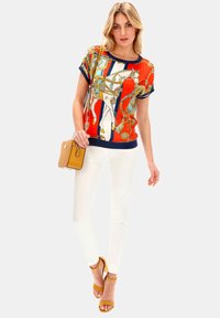 Czerwono-niebieska top z krótkim rękawem w wzór, z białym wzorem konia, sparowany z białymi spodniami i żółtymi sandałami. W komplecie mała torebka w kolorze brązowym.