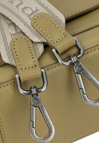 Borsa in pelle beige con tracolla decorata, clip in metallo argento e dettagli cuciti. Tessuto liscio con un design strutturato.