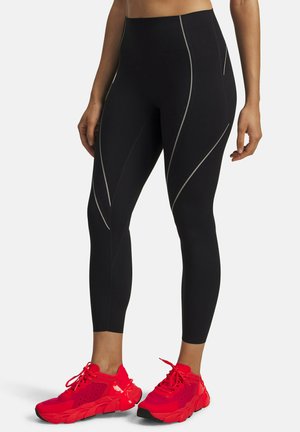 Black high-waisted leggings with reflective piping details, paired with bright red athletic shoes featuring a textured upper and black soles.