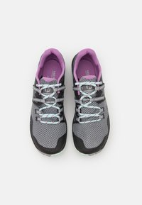 Zapatillas de trail running en malla gris con acentos negros. Presentan un forro interior morado y cordones azul claro con detalles en rosa. Suela de goma.