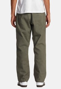 Olijfgroene katoenen broek met een ontspannen pasvorm, voorzien van zijzakken en een gladde textuur, gecombineerd met zwart-witte sportschoenen.