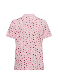 Poloshirt aus hellrosa Stoff mit einem Muster aus kleinen roten Herzen, kurzärmlig und mit Kragen. Die Rückansicht zeigt das gesamte Design.