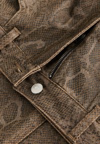 Brązowa kurtka w wzór skóry węża, z srebrnym zatrzaskiem, lamówką na zamek błyskawiczny oraz teksturowaną tkaniną o subtelnym połysku.