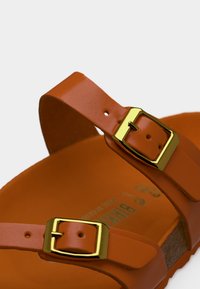 Πορτοκαλί σανδάλι με δύο ρυθμιζόμενους ιμάντες που διαθέτουν αγκράφες από μέταλλο σε χρυσό τόνο και διαμορφωμένο πάτο από φελλό.