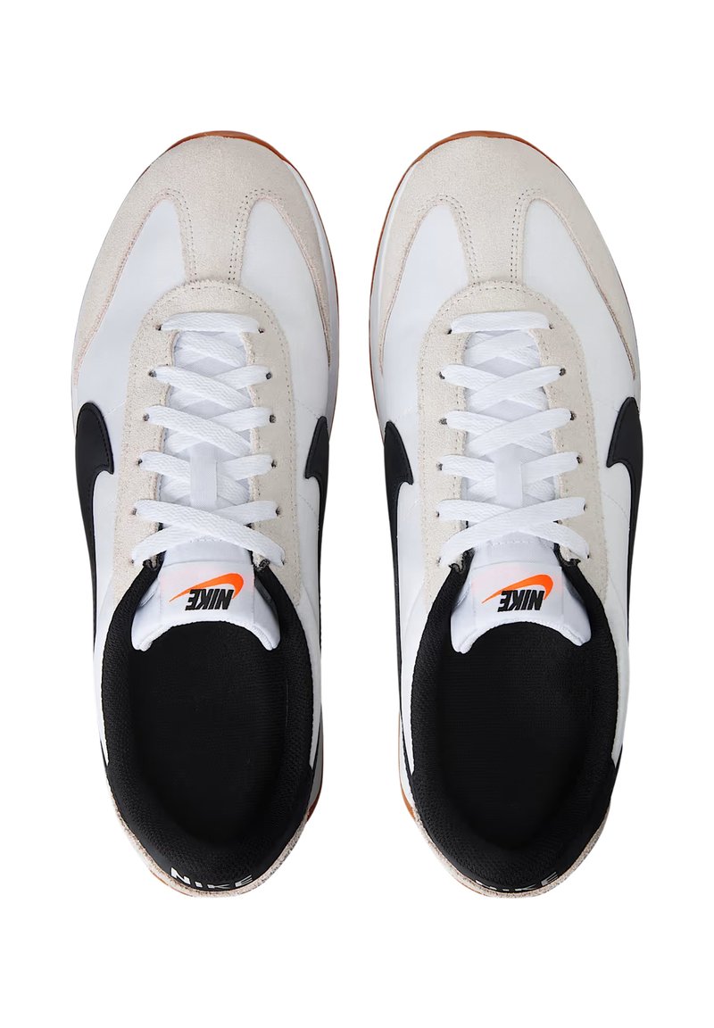 Zapatillas Nike en blanco y negro con un acento de gamuza, presentando cordones blancos, punta redonda y suela de goma con un logo naranja en el interior.