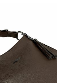 Bruine handtas van gestructureerd leer met een metalen merkembleem en een leren kwastje bevestigd aan een metalen ring aan de schouderband.