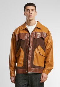 Braune und beige Jacke aus Leder und Cord, mit Knopfleiste, mehreren Taschen und kontrastierenden Texturen an Ärmeln und Körper.