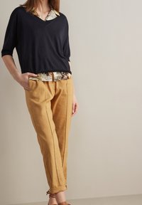 Námořnický top s V výstřihem vrstvený přes květinovou košili s límečkem, spárovaný s hořčicovými lněnými kalhotami se bočními kapsami a vertikálními švy. Hnědé sandály.