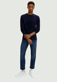 Navy sweater with long sleeves paired with blue jeans. The outfit is completed with white sneakers and a relaxed fit. Smooth texture throughout.