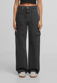 Pantalons cargo gris foncé à taille haute, dotés de grandes poches latérales, d'une coupe ample et d'une conception à jambes droites. Portés avec des baskets blanches.