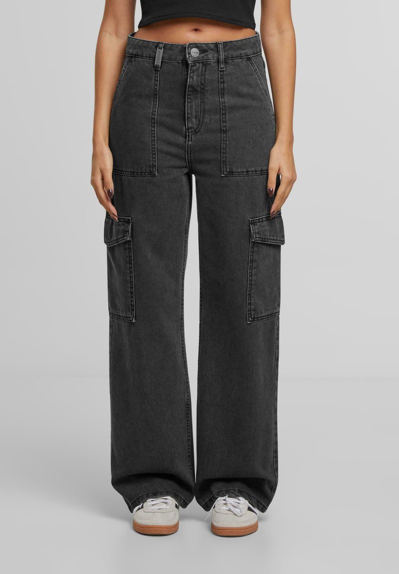 Pantalons cargo gris foncé à taille haute, dotés de grandes poches latérales, d'une coupe ample et d'une conception à jambes droites. Portés avec des baskets blanches.