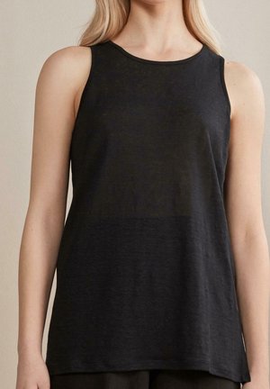 Femme portant un débardeur noir sans manches avec un col rond, sur un fond neutre.