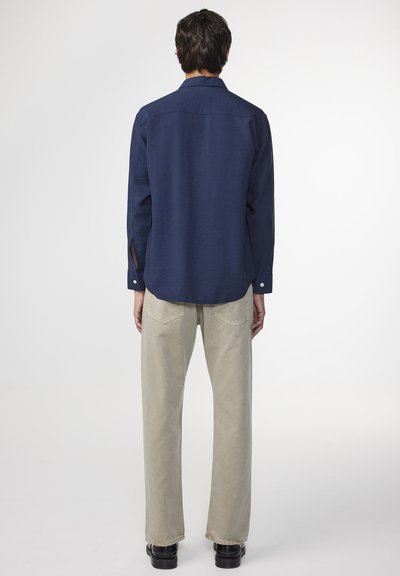 Navy long-sleeve shirt with a textured finish, buttoned cuffs, and a relaxed fit. Paired with beige, straight-leg trousers and black shoes.