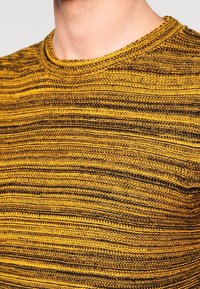 Žlutý a černý pruhovaný pletený svetr s kulatým výstřihem, vyrobený z texturované látky a s těsným střihem.