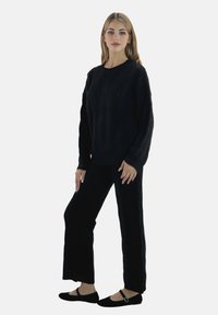 Sort strikket sweater med kabelmønster, kombineret med matchende sorte bukser med vide ben. Modellen har sorte flade sko med rem.