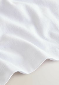 Biała bawełniana tkanina o miękkiej teksturze, z delikatnymi falami i widocznym przeszyciem wzdłuż krawędzi. Prosty i gładki design.