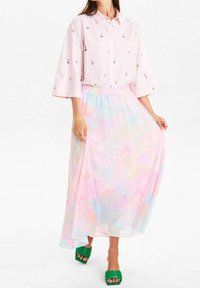 Camicia collared rosa chiaro con ricami floreali, abbinata a una gonna plissettata pastello lunga fino al pavimento con motivi astratti. Tacchi a blocco verdi.