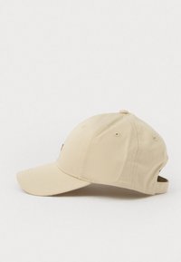 Beige baseballová čepice s prohnutým krempou, vyrobená z měkké tkaniny. Obsahuje ventilační otvory a nastavitelný pásek vzadu.