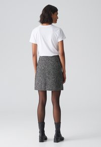 Weißes T-Shirt mit kurzen Ärmeln, kombiniert mit einem strukturierten Rock in Schwarz-Weiß im Fischgrätmuster, abgerundet mit schwarzen Stiefeletten und transparenten Strumpfhosen.