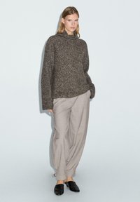 Chunky, donkergrijze gebreide trui met een hoge hals, gecombineerd met lichtgrijze, loszittende broek en zwarte instap schoenen.