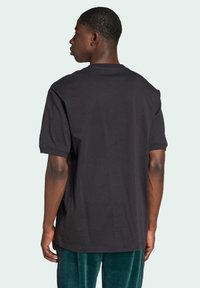 Černé tričko s krátkým rukávem z bavlny, s kulatým výstřihem a volným střihem. Hladká textura, žádné viditelné vzory ani grafiky.