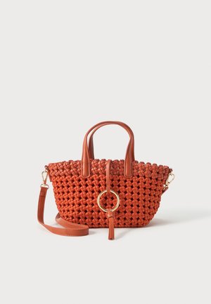 Borsa intrecciata arancione ruggine con manici corti, tracolla staccabile e grande anello dorato con dettaglio nappina sul davanti.