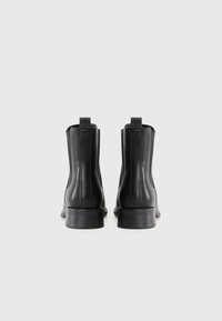 Botas de tobillo de cuero negro con una textura suave, presentan paneles elásticos en los laterales, tiradores y un tacón bajo.