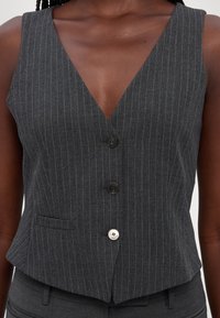 Grå randig väst med V-hals, två knappar och en sidficka. Tyget har en slät struktur och är skräddarsydd för en perfekt passform.