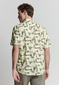 Korte mouwen shirt met een lichtgroen en beige abstract patroon met geometrische vormen; gemaakt van een lichtgewicht stof, met een knoopsluiting bij de kraag.