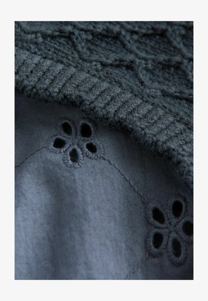 Tamsus mezgimo megztinis su tekstūruota danga, atskleidžiančia lygų tamsų audinį po juo, puošniu gėlių siuvinėjimu ir mažomis išpjovomis.