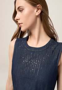 Denim-toppi, jossa on pyöreä kaula-aukko ja pystysuoria metallikoristeluja tekstuuria varten, syvän sinisessä värissä.