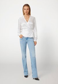 Balta sateninė palaidinė su ilgomis rankovėmis, apykakle, derinama su šviesiai mėlynomis platėjomis džinsomis ir juodomis smailiomis aukštakulnėmis bateliais.