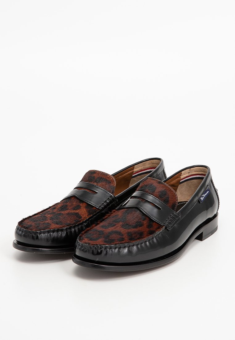 Mocassins à motif léopard marron et noir avec un élégant bord en cuir noir et une semelle en caoutchouc. Dotés d'une sangle décorative sur le dessus.