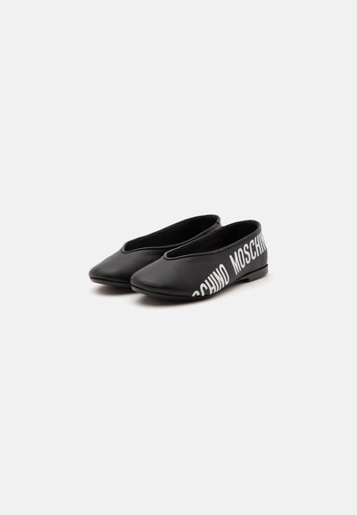Paire de chaussures plates noires slip-on à bouts pointus avec le texte blanc « MOSCHINO » sur le côté extérieur de la zone du talon.