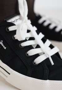 Mustad mustad sneakers, valgete paelte ja valge tallaga. Küljel on logo ja taldadel paralleelsed triibud.